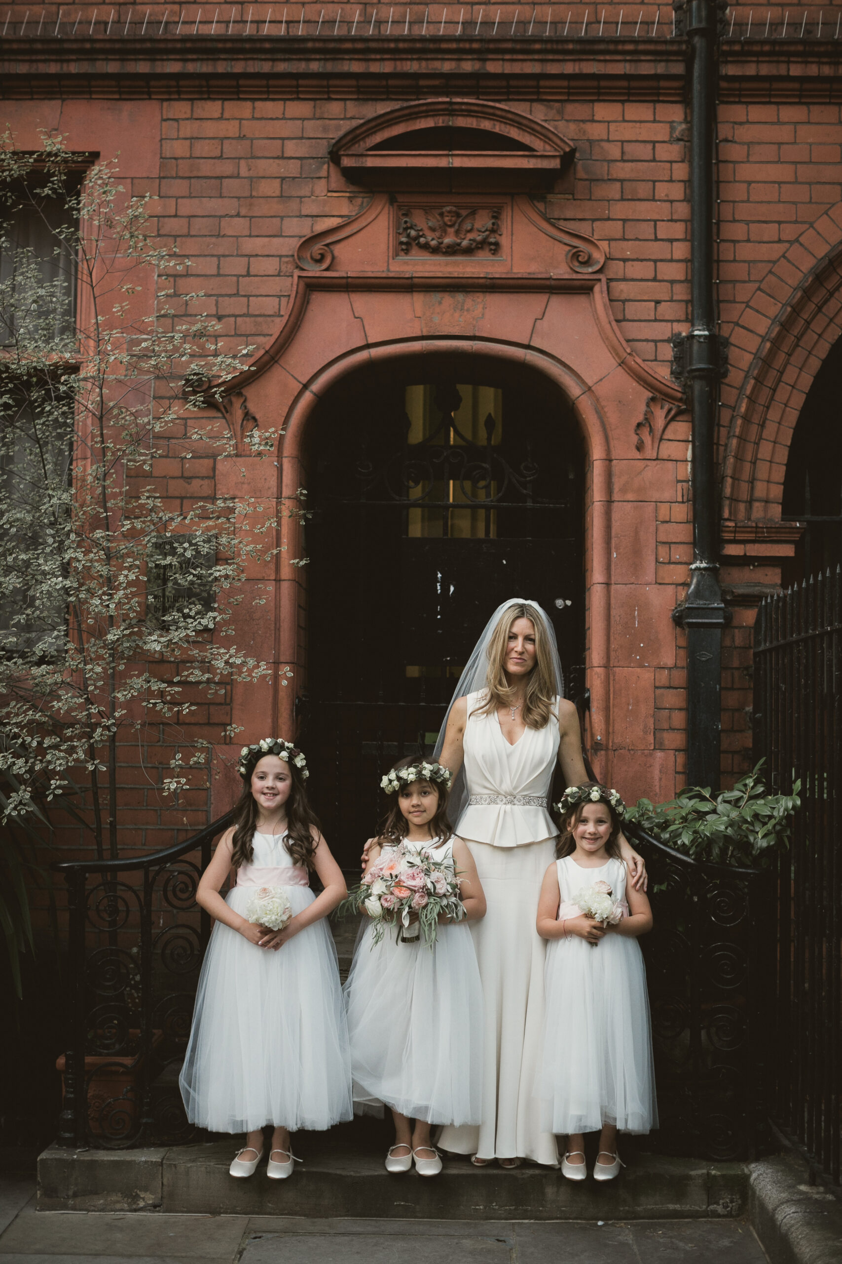 A photo of a group of flower girls wearing an ivory tulle dress with an oversized pink silk sash