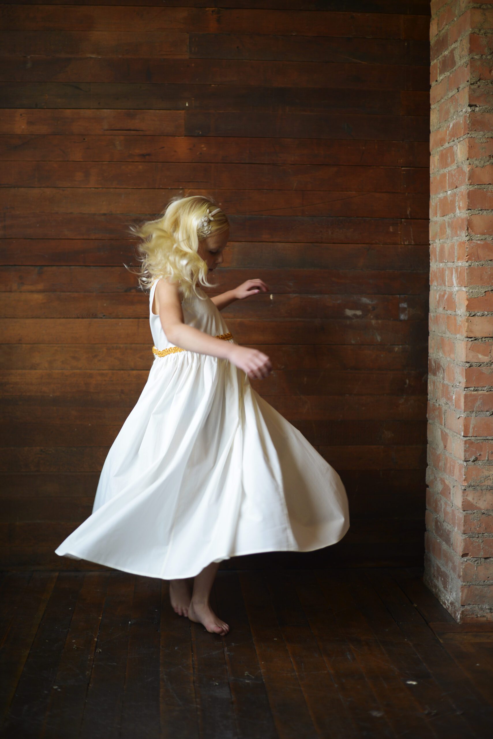 A photo of a flower girl in an ivory cotton dress with gold trim