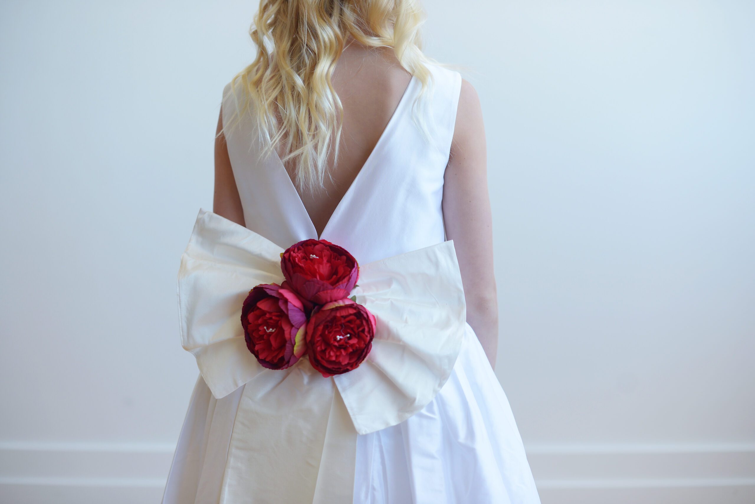 A picture of an ivory flower. girl dress in pure cotton or handmade in silk with an oversized red silk flower bow.