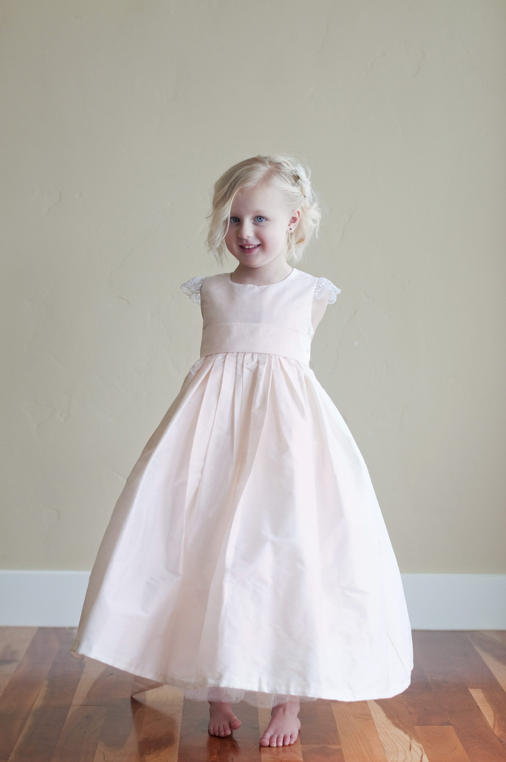 A photo of a pure silk flower girl dress in blush pink with lace sleeves