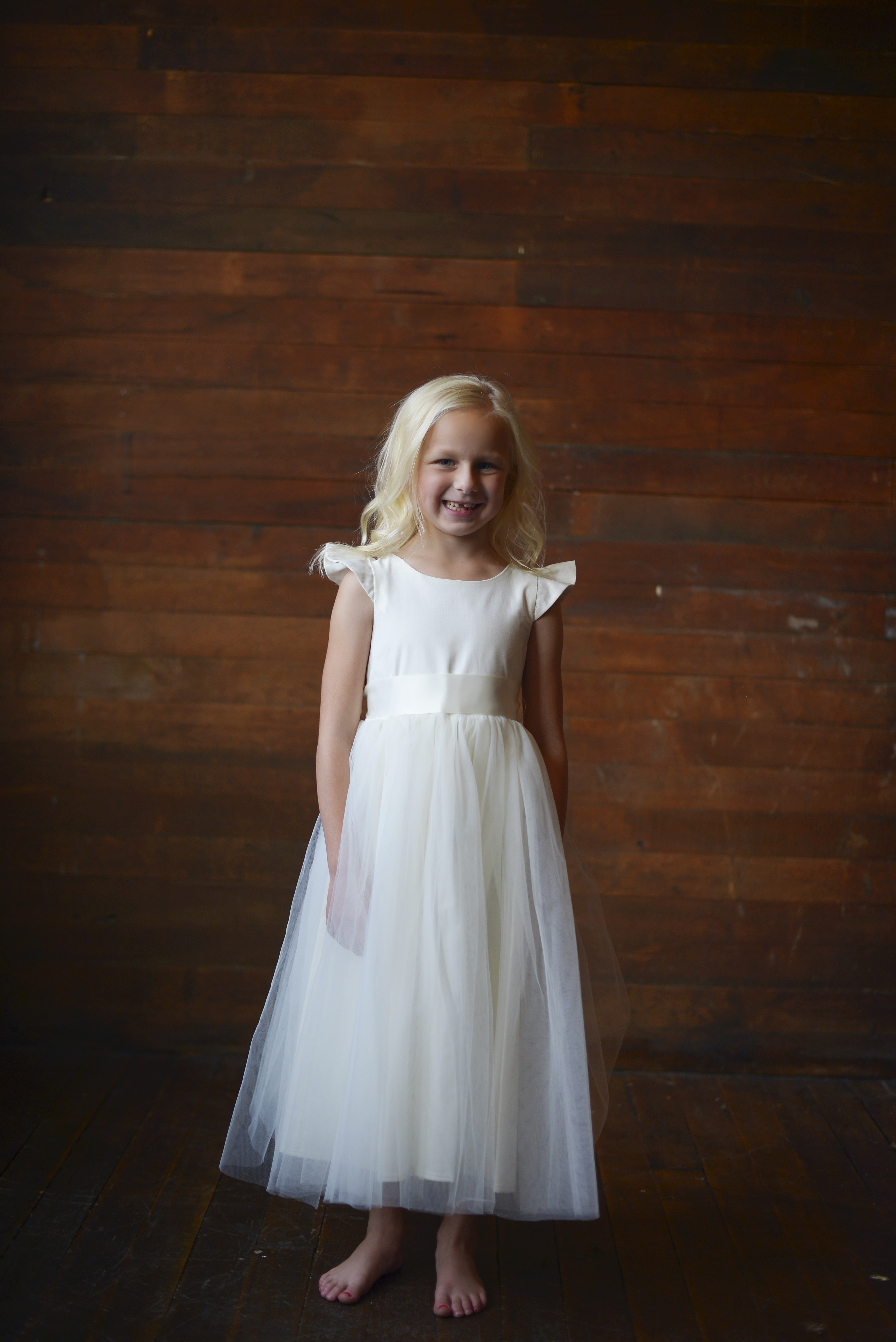 A photo of a girl wearing an ivory hand made to measure flower girl dress in ivory or white with a tulle skirt