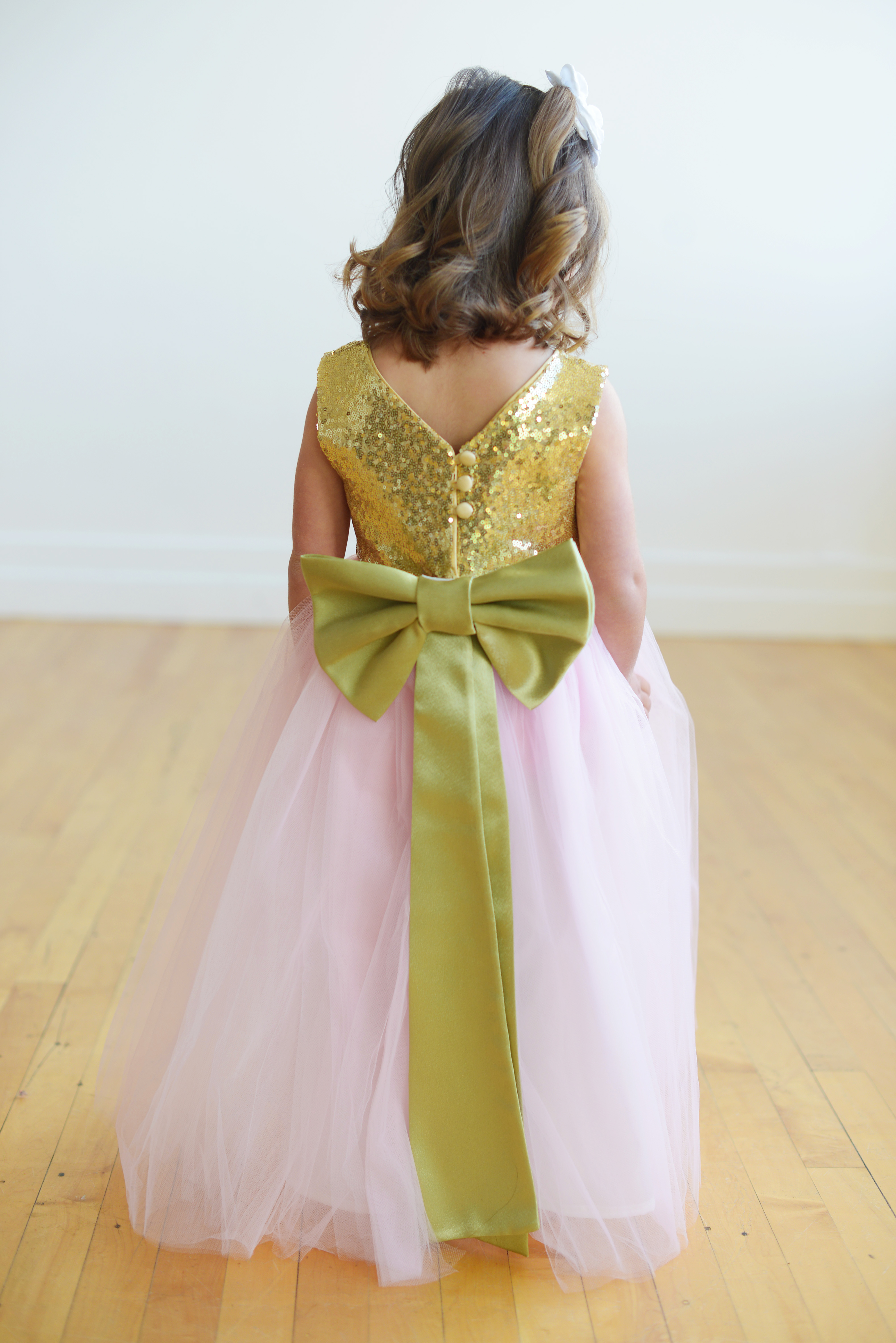 A photo of the back of a gold sequin flower girl dress with a pink tulle skirt