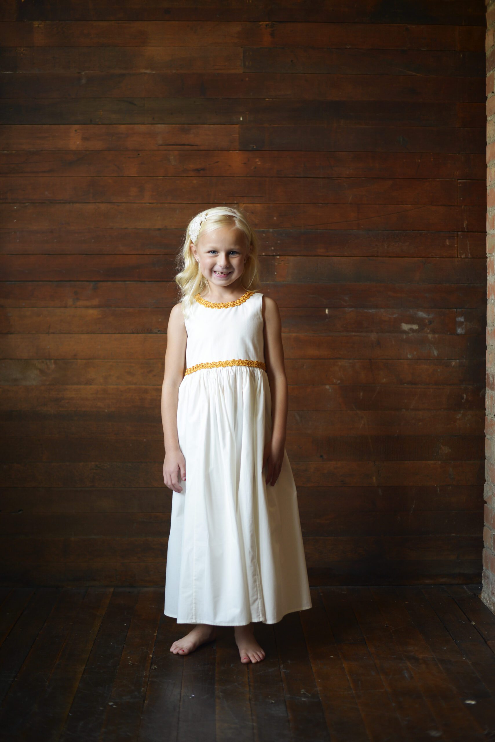 A photo of a girl wearing an ivory flower girl dress with gold brocade trim