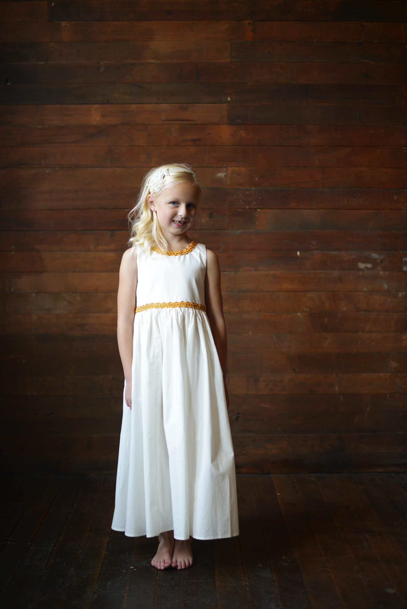 A girl wearing an ivory and white flower girl dress with gold brocade trim