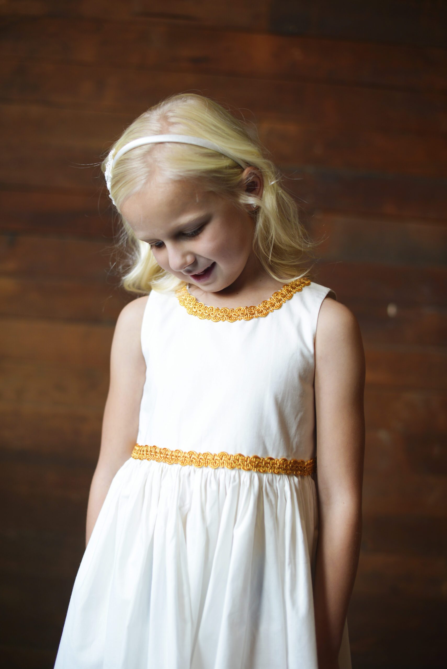 A photo of a 6 year old flower girl wearing a cotton dress with gold brocade around the waist