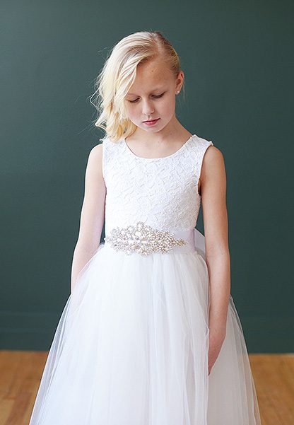 A white lace flower girl or first communion dress with a full sash