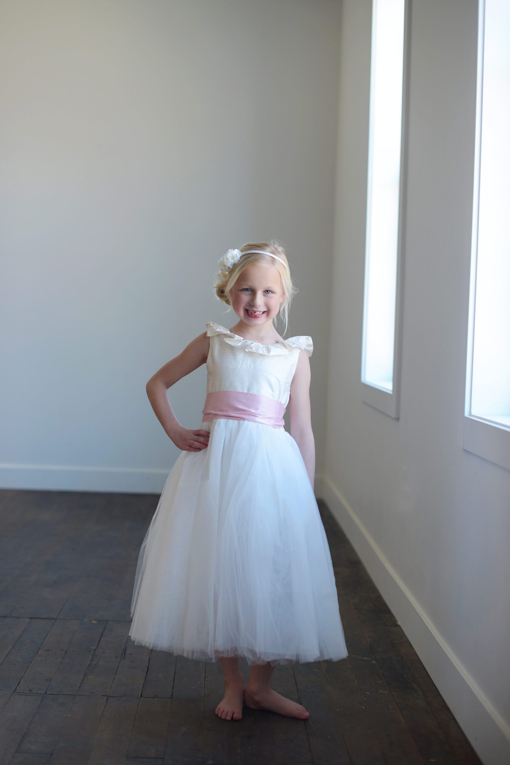 A photo of a flower girl wearing a made to measure silk and tulle slower girl dress with a pink sash