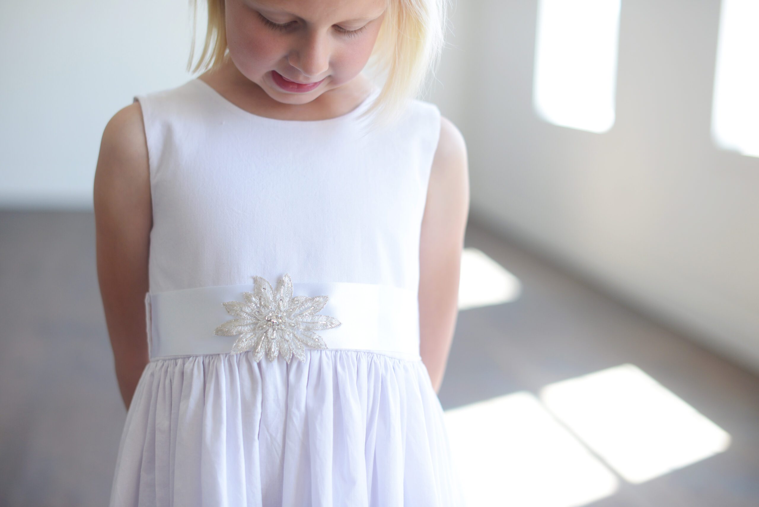 A white cotton flower girl dress with a diamante sash