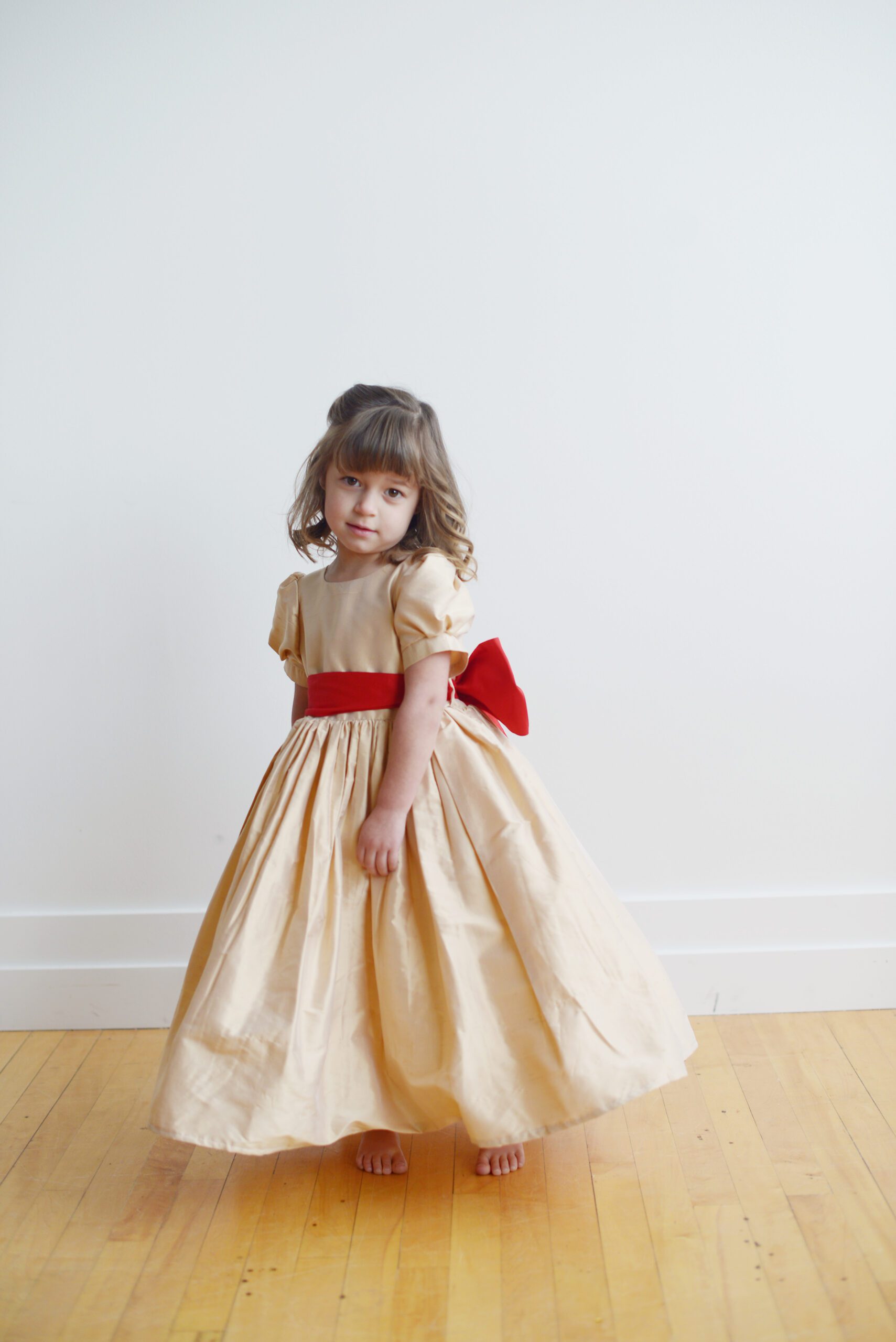 A photo of a flower girl wearing a pure silk dress in champagne with a red oversized bow