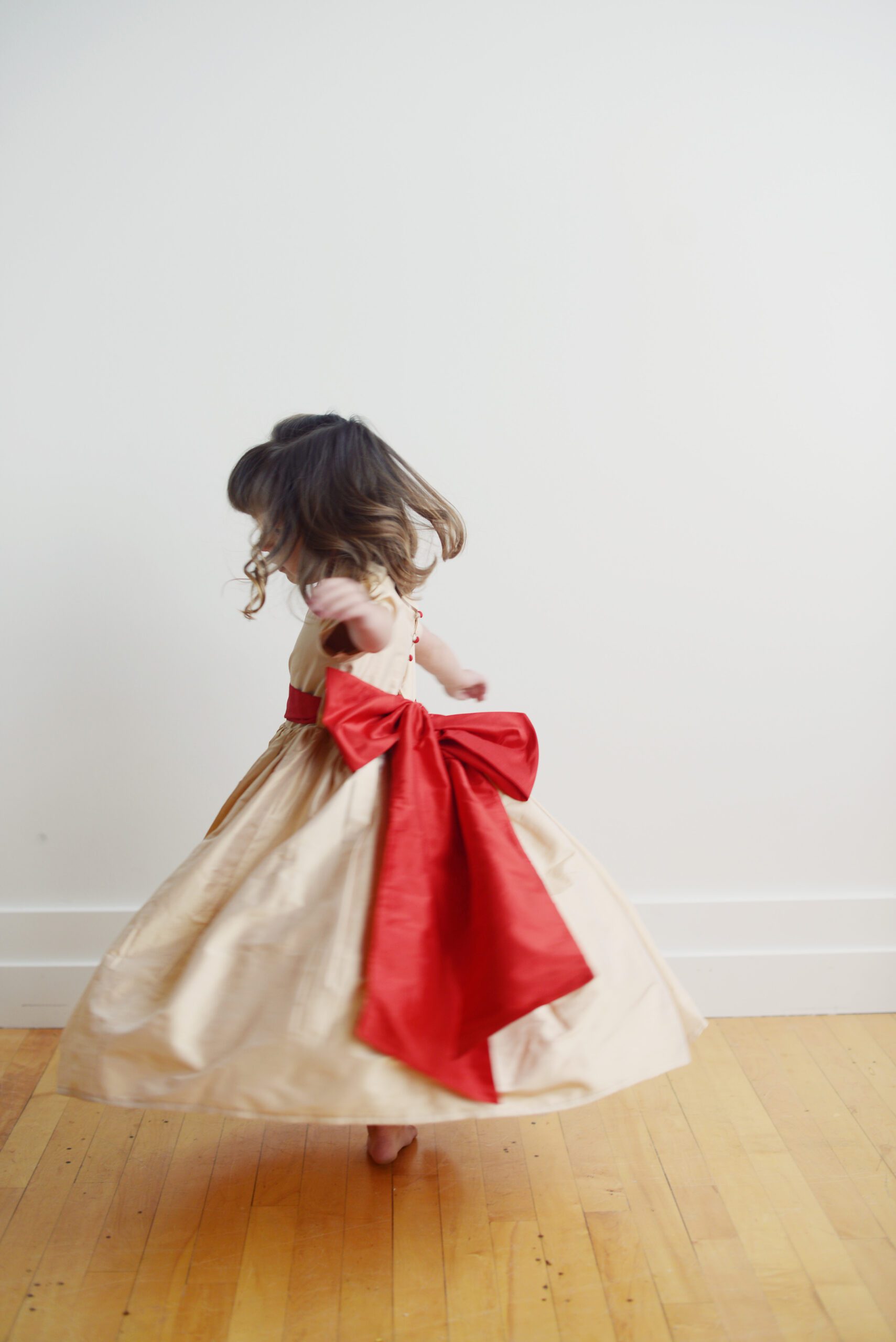 A photo of a flower girl dancing and wearing a pure silk dress in champagne with a red oversized bow