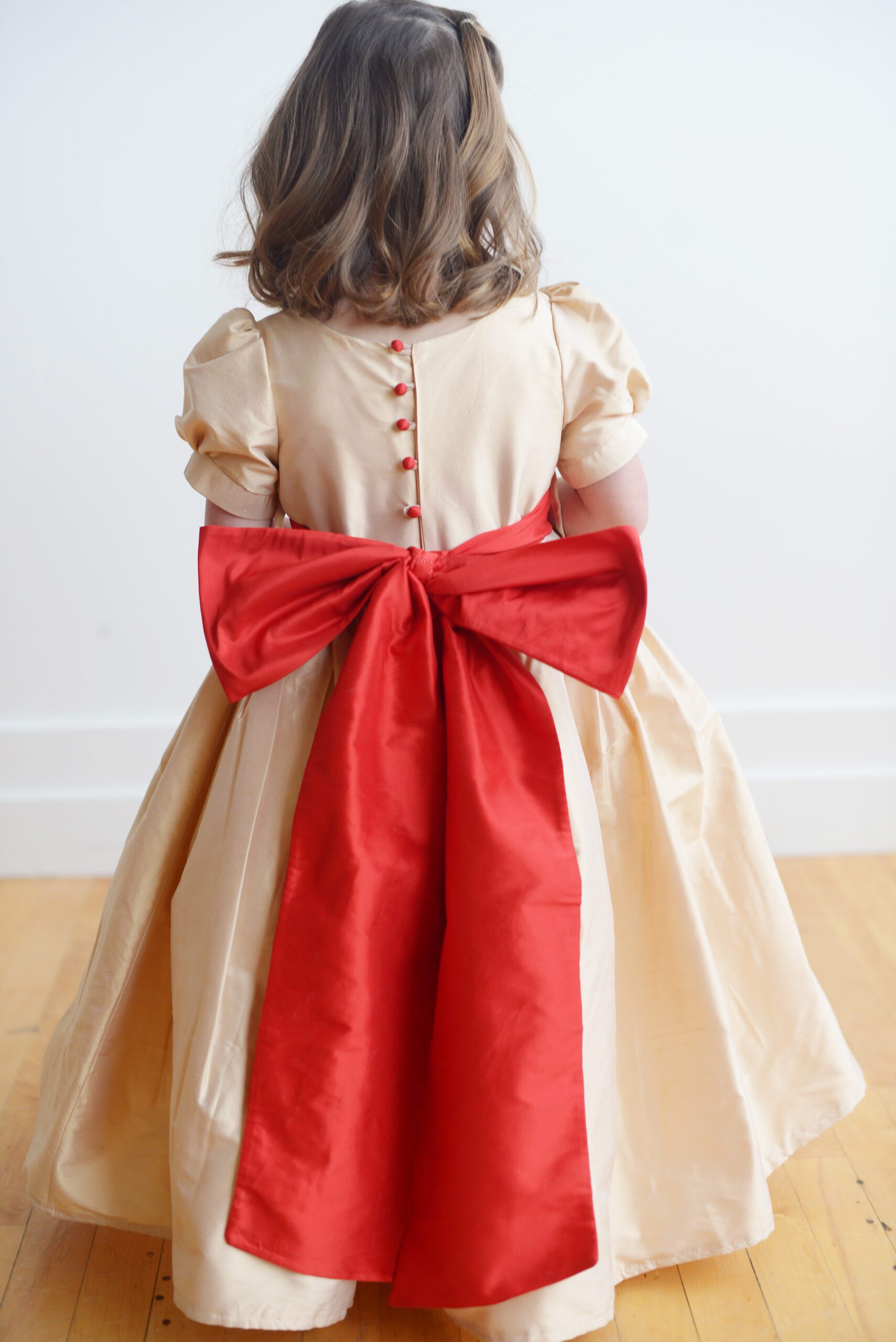 A silk champagne flower girl dress with sleeves and a bow.