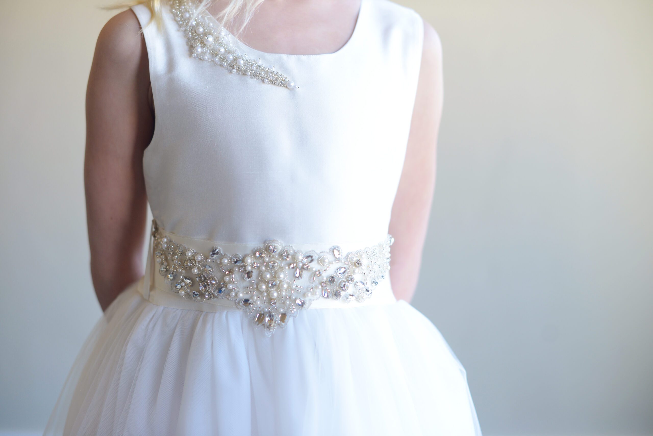 A photo of a girl wearing a silk flower girl dress with a pearl and diamante motif on the shoulder