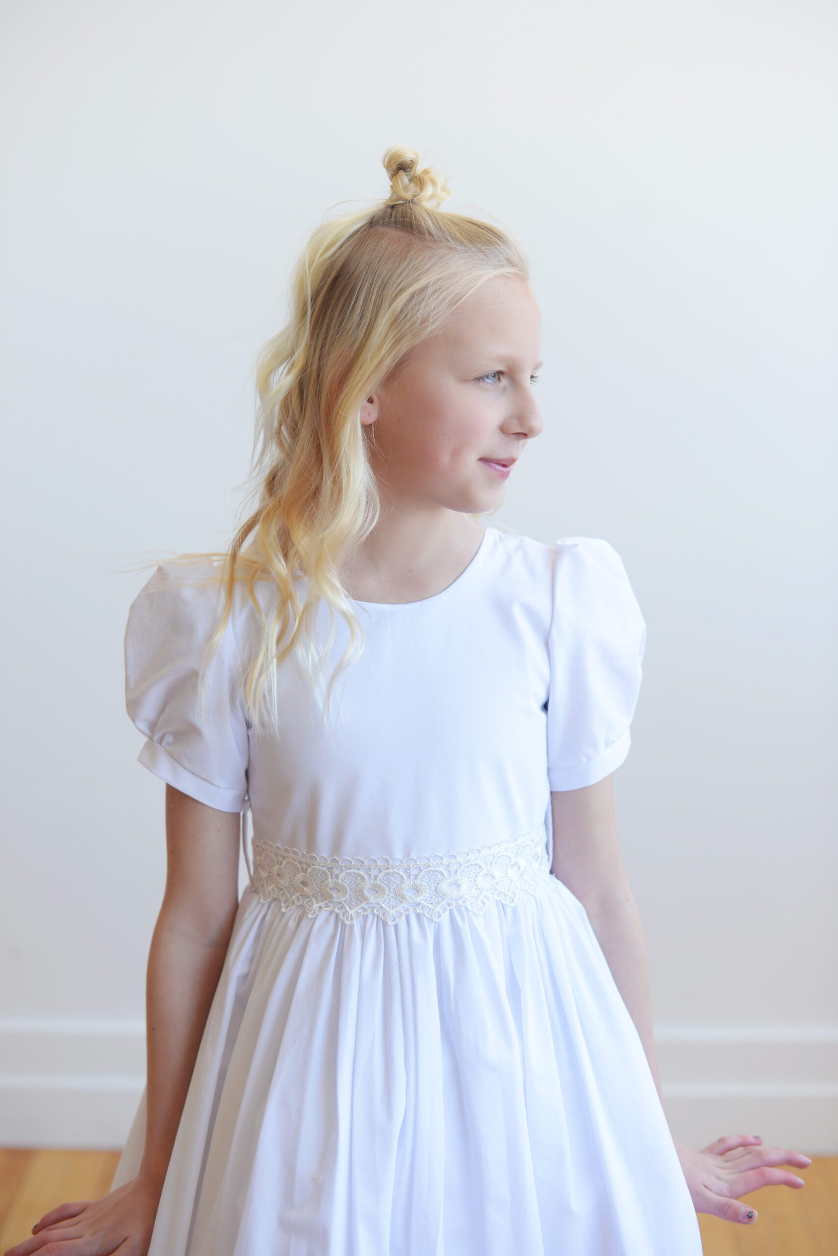 A photo of a white cotton first communion dress with a lace sash