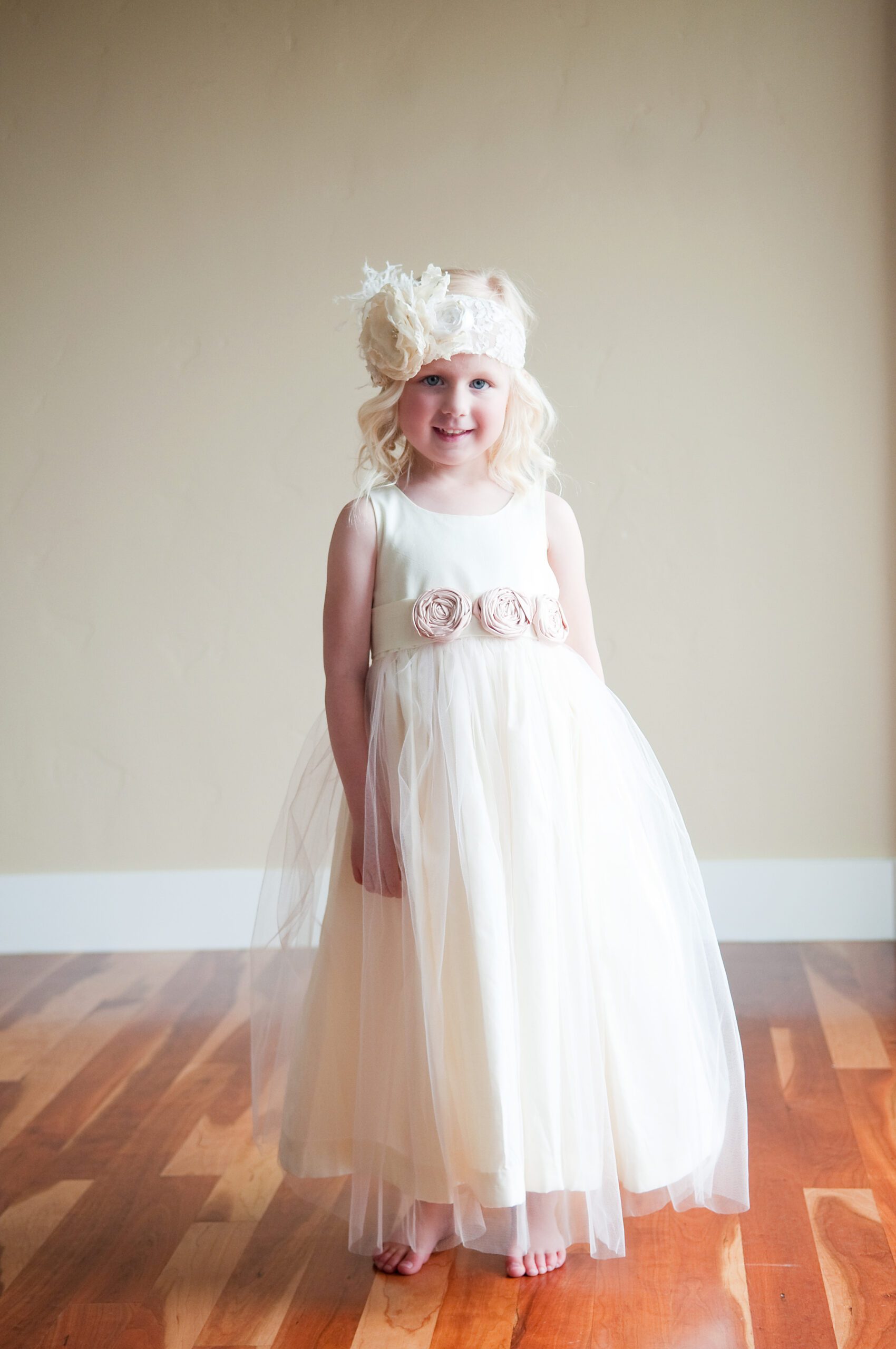 A photo of of a young flower girl in an ivory cotton dress with tulle on the skirt and pink flowers