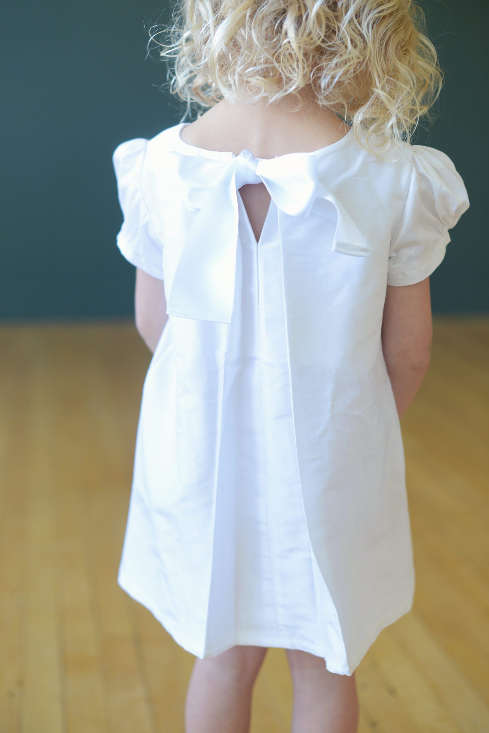 A photo of the back of a white silk flower girl dress with a bow at the collar
