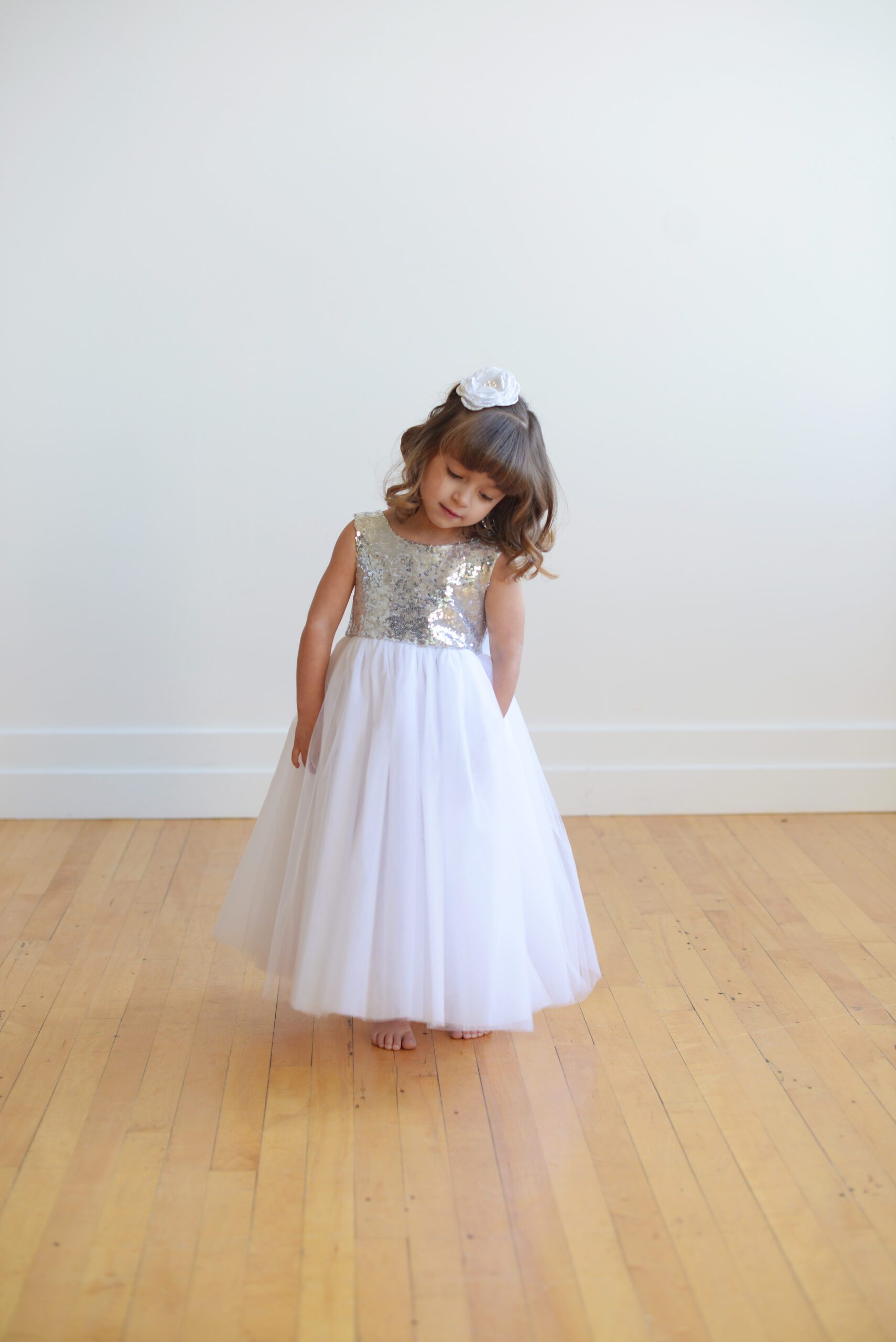A photo of a little girl wearing a silver sequin flower girl dress with a silk sash