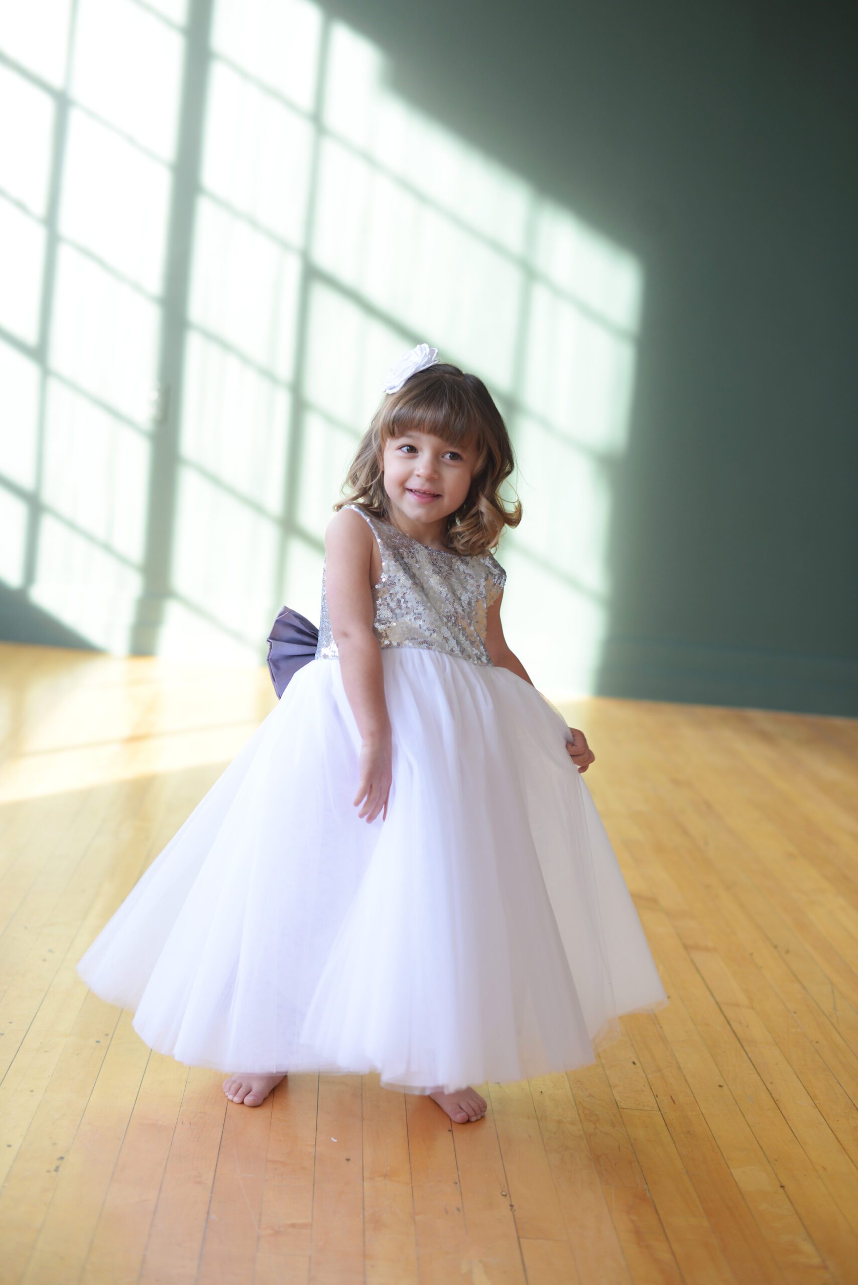 A photo of a little girl wearing a silver sequin flower girl dress with a silk sash in purple