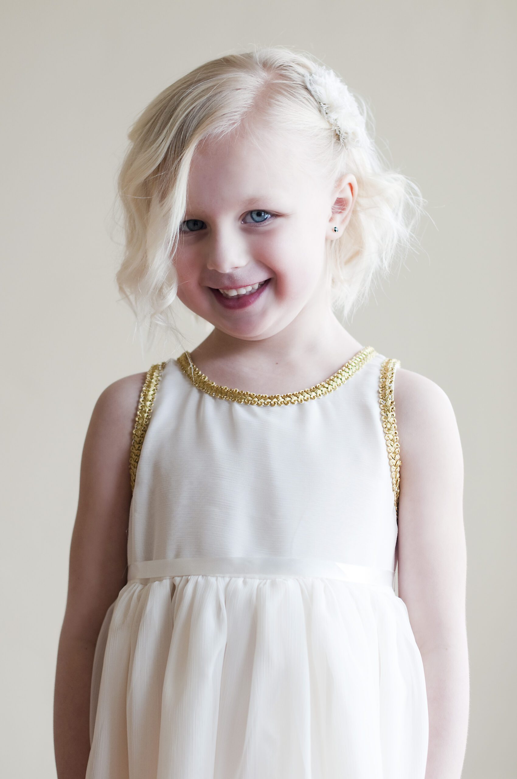 A photo of a little flower girl wearing an ivory chiffon dress with gold brocade on the collar