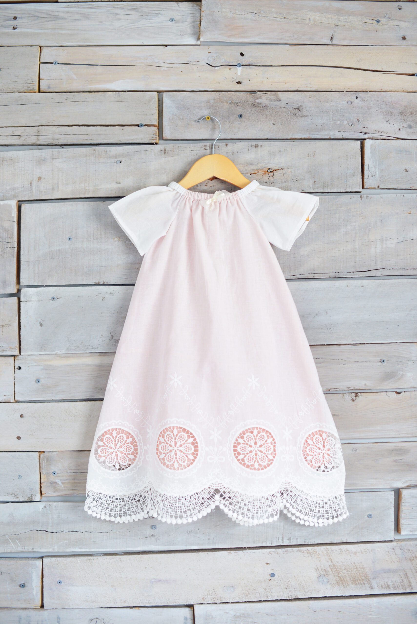 A photo of a white lace christening gown with a pink underlay