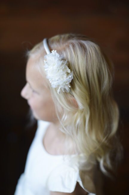 A photo of a flower girl wearing a floral head band in white