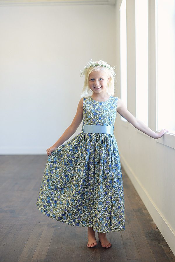A photo of a flower girl wearing a blue floral dress with an ivory sash
