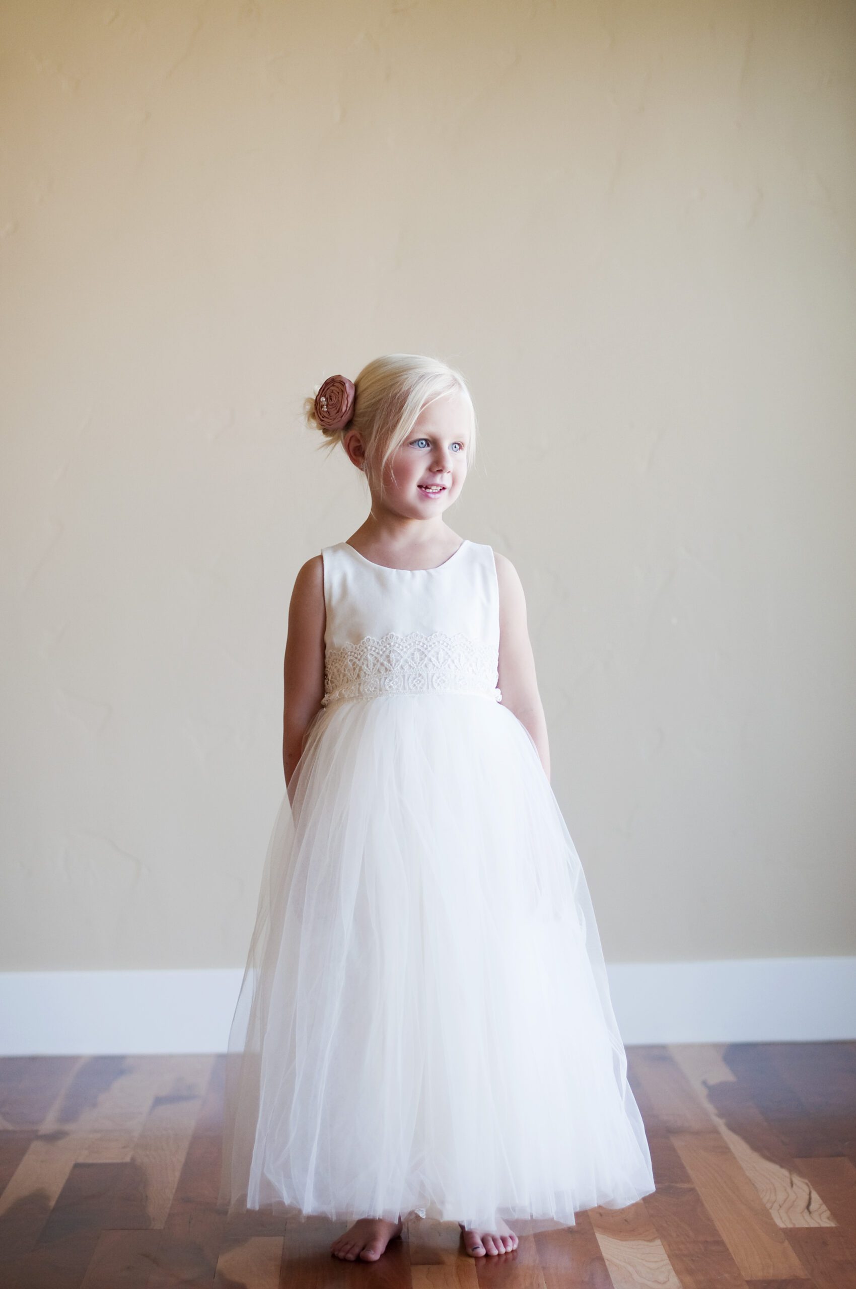 A photo of a young flower girl wearing a white cotton and tulle flower girl dress with a pink silk flower