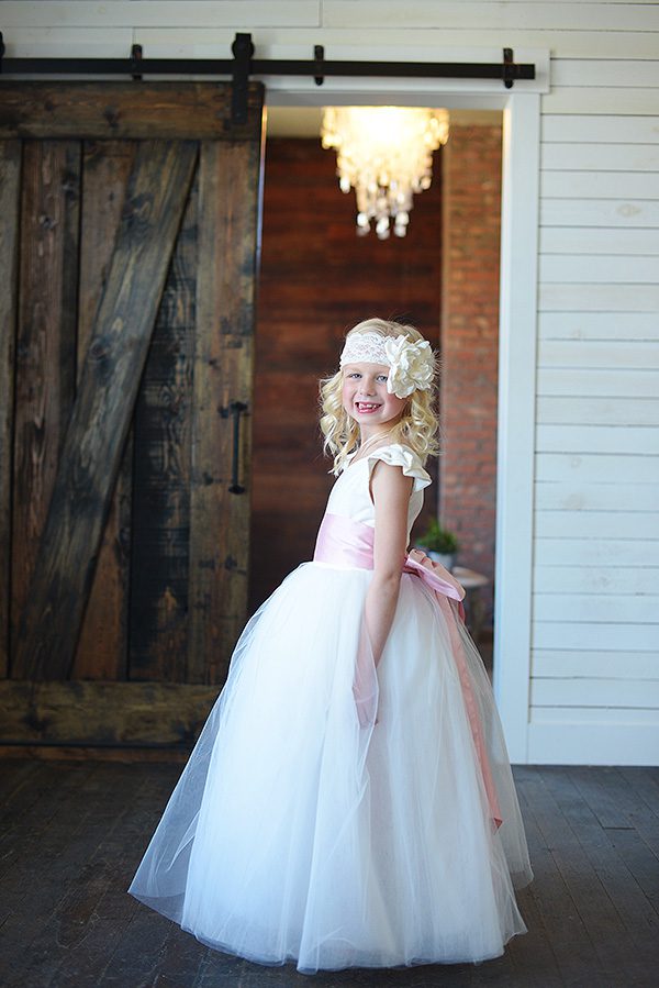 A photo of a cotton and tulle flower girl dress with a very full tulle skirt and a pink sash