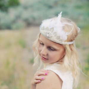 A photo of a flower girl wearing a feathered tiara and a flower girl dress with a full tulle skirt