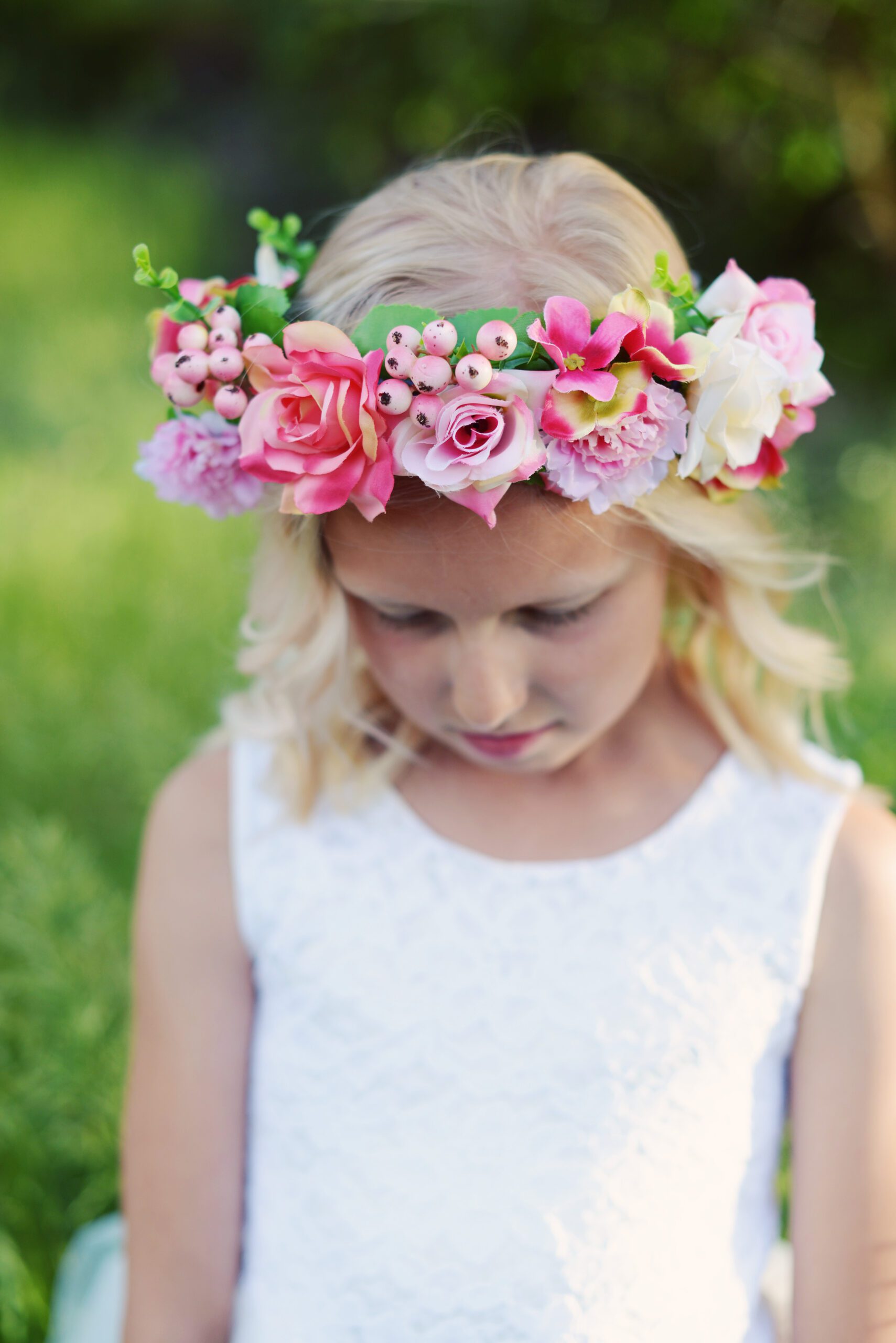 A photo of a flower girl wearing a pink and red rose flower girl crown and a white flower girl dress in silk and tulle