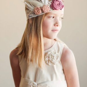 A photo of a flower girl wearing a lace headband with pearls and a pink silk flower in a 1920's style