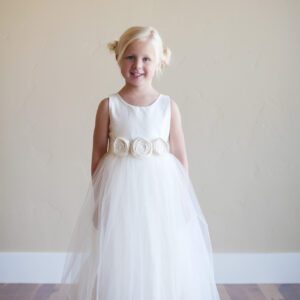 A photo of an ivory flower girl dress in cotton with a floral sash and a tulle skirt