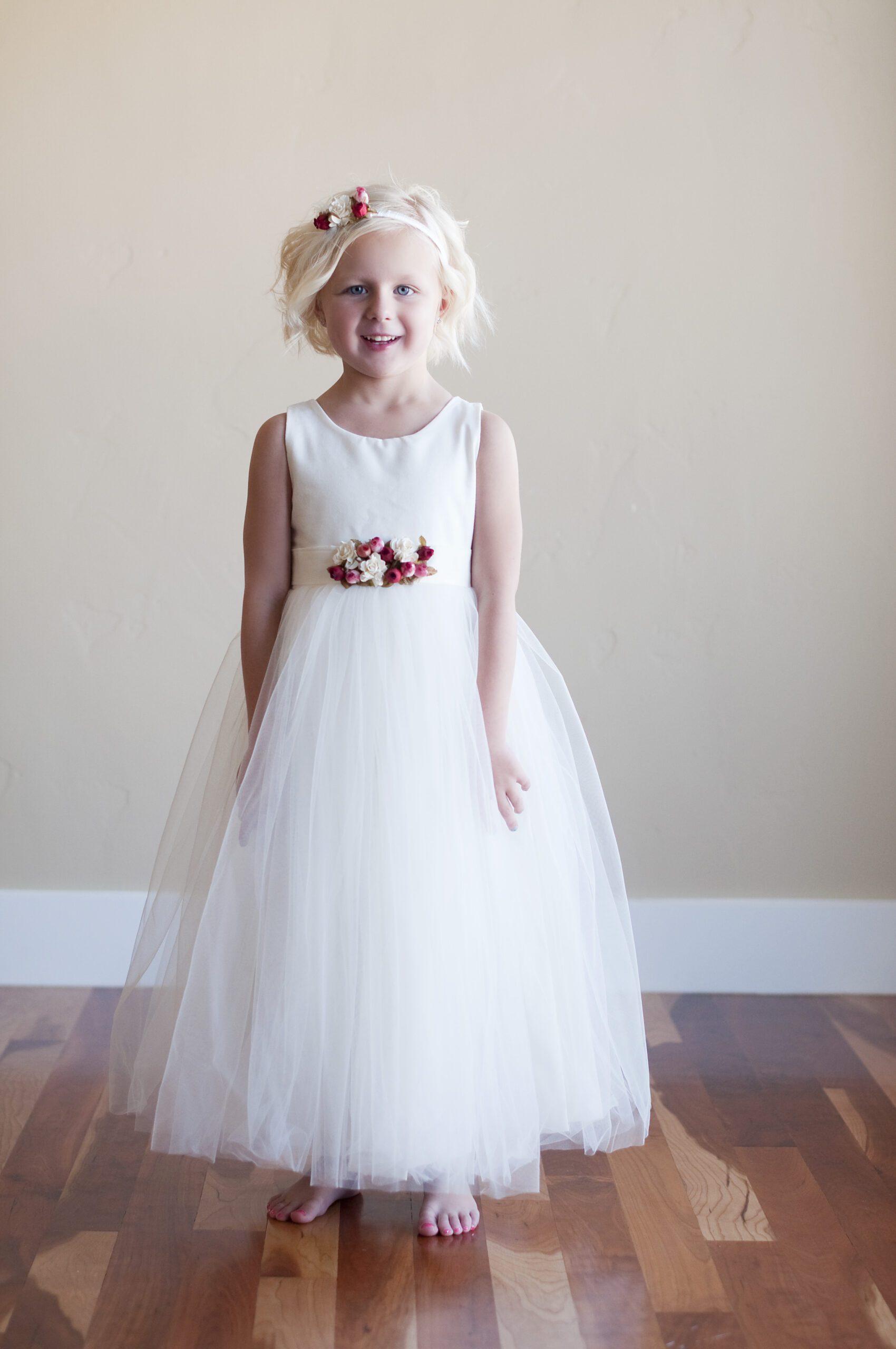 A photo of a flower girl wearing a cotton and tulle dress with pretty red roses