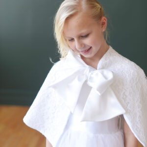 A photo of a girl wearing a lace communion cape which ties in a bow at the neck