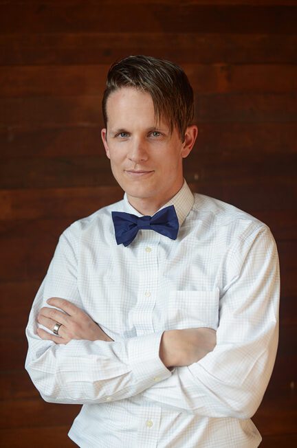 A photo of a man wearing a navy silk bow tie with a white shirt