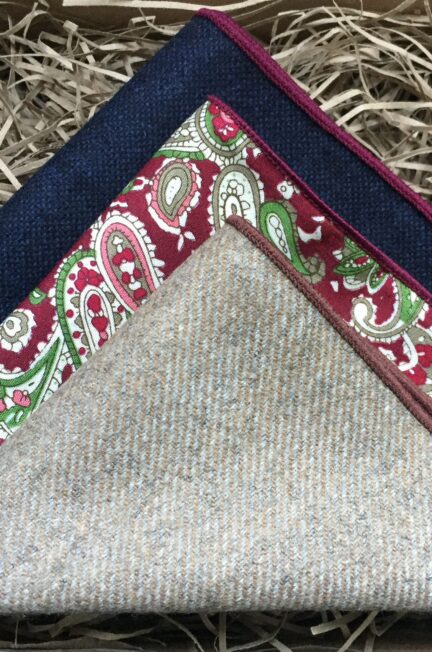 A photo of three pocket squares in navy wool, paisley cotton and beige wool