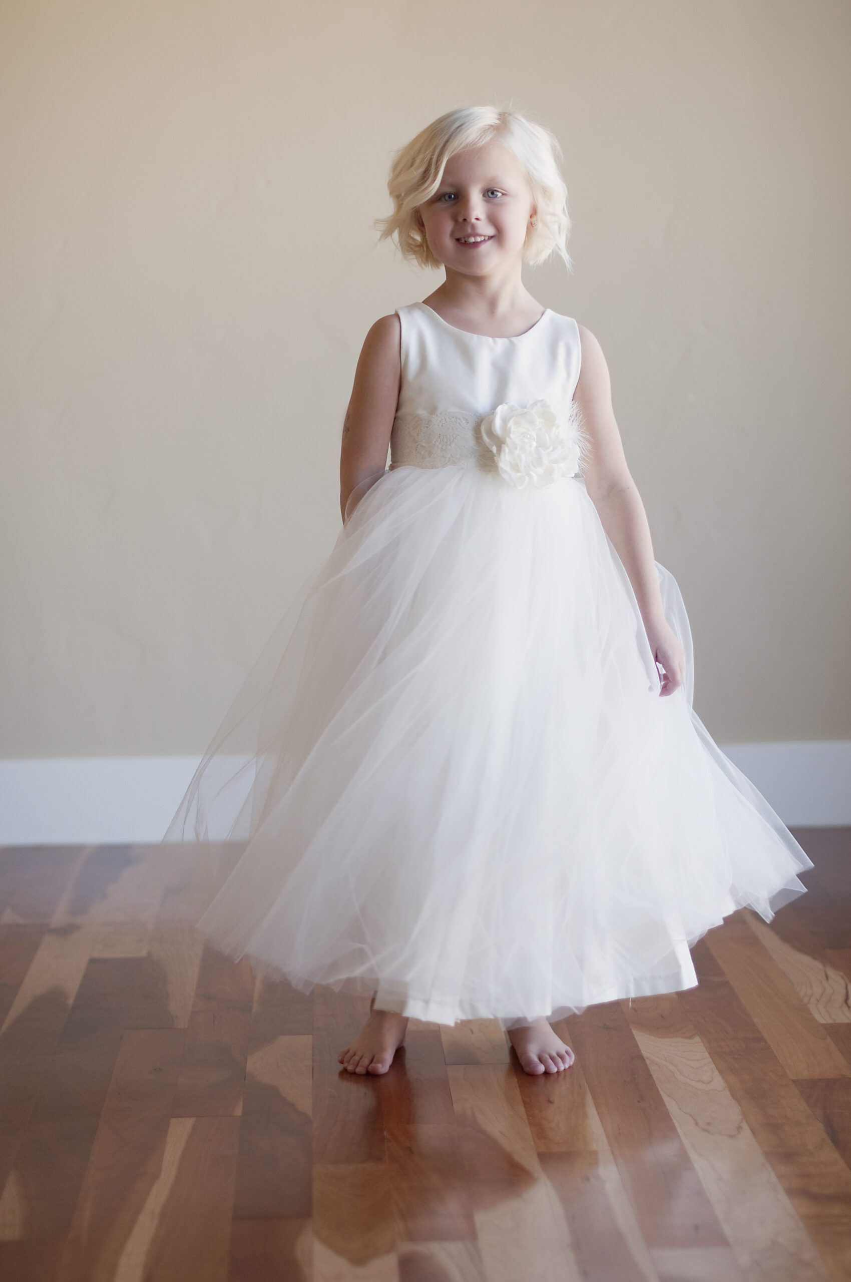 A photo of a 4 year old flower girl wearing a nivory dress with a ailk bodice and a full tulle skirt with an over sized flower on a lace sash