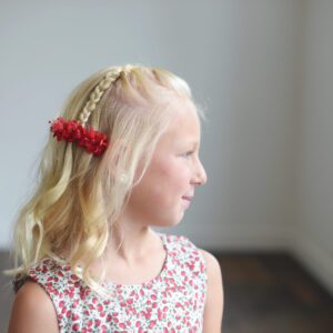 A photo of a flower girl wearing a red flower girl hair clip in her hair