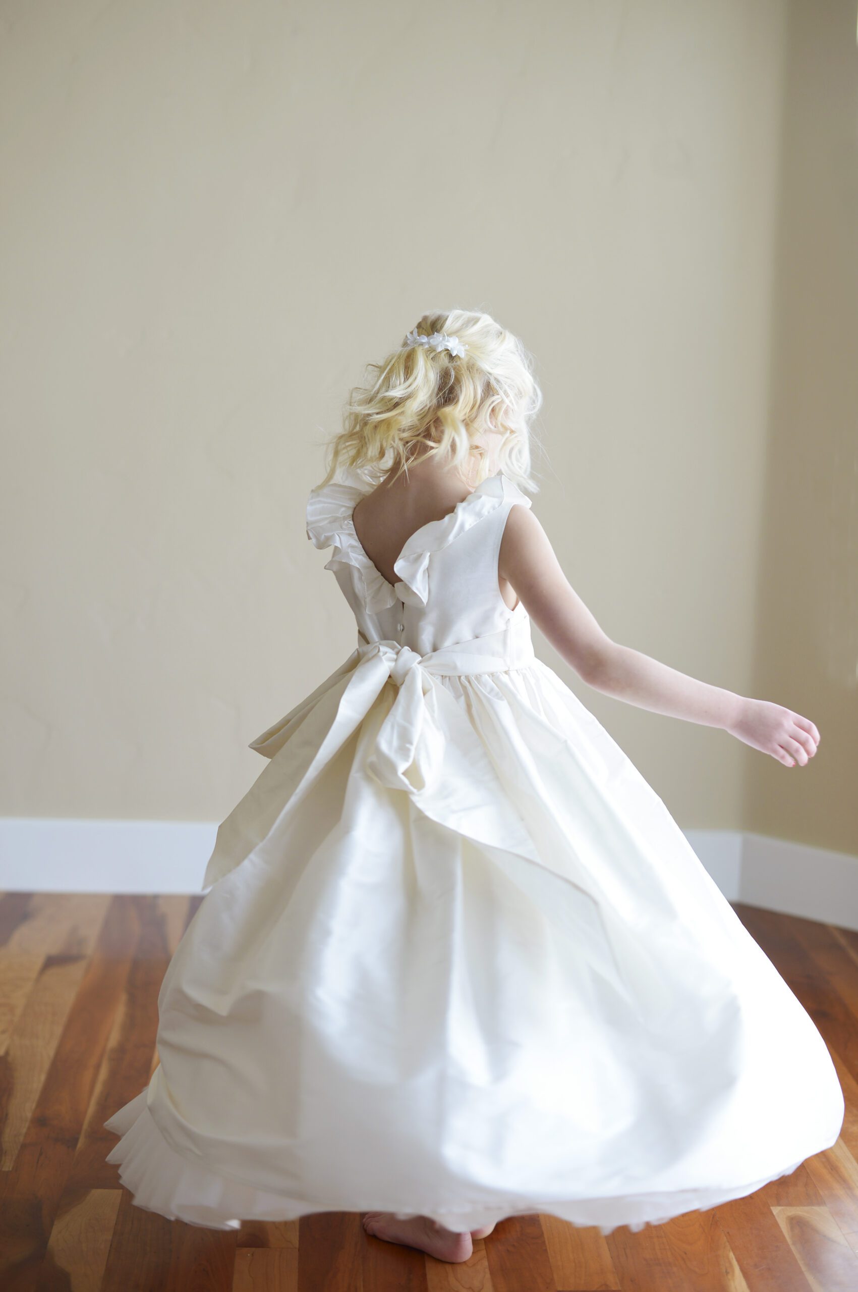 A photo of a white silk flower girl dress with a v back and ruffle collar and sash