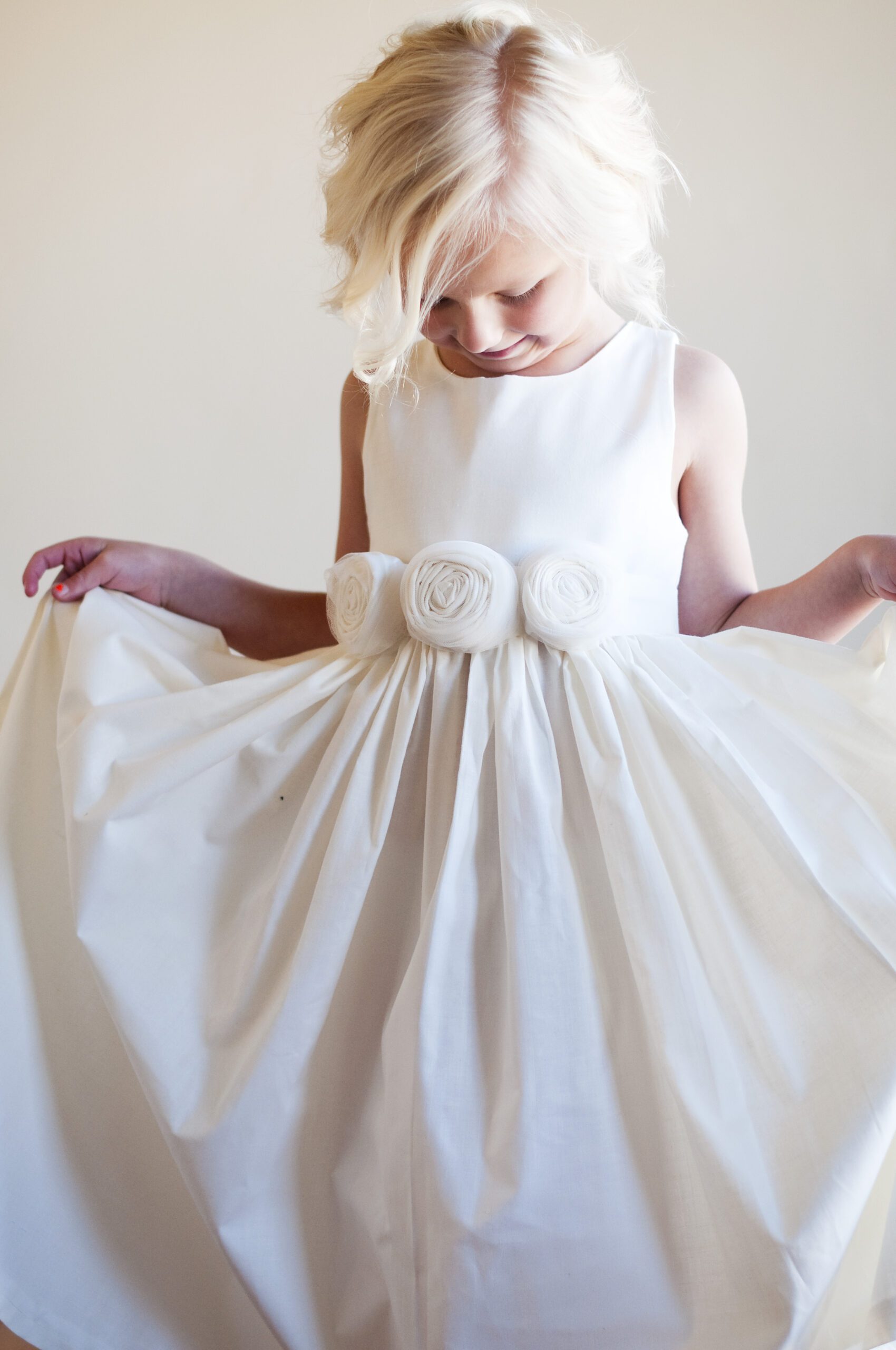 A young flower girl wearing a cotton flower girl dress with three pretty roses on the sash
