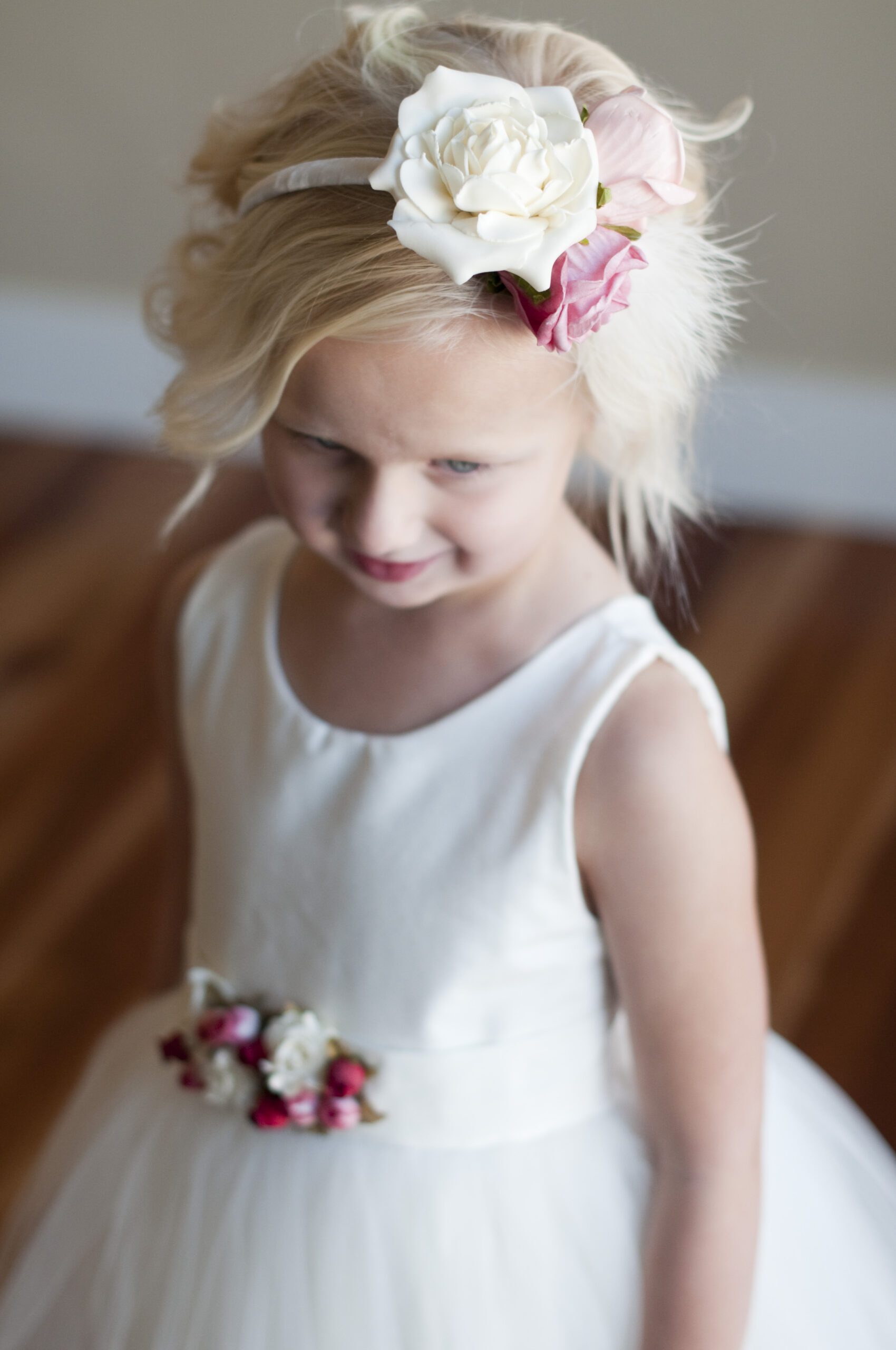 A photo of a flower girl wearing a pink floral headband and an ivory dress