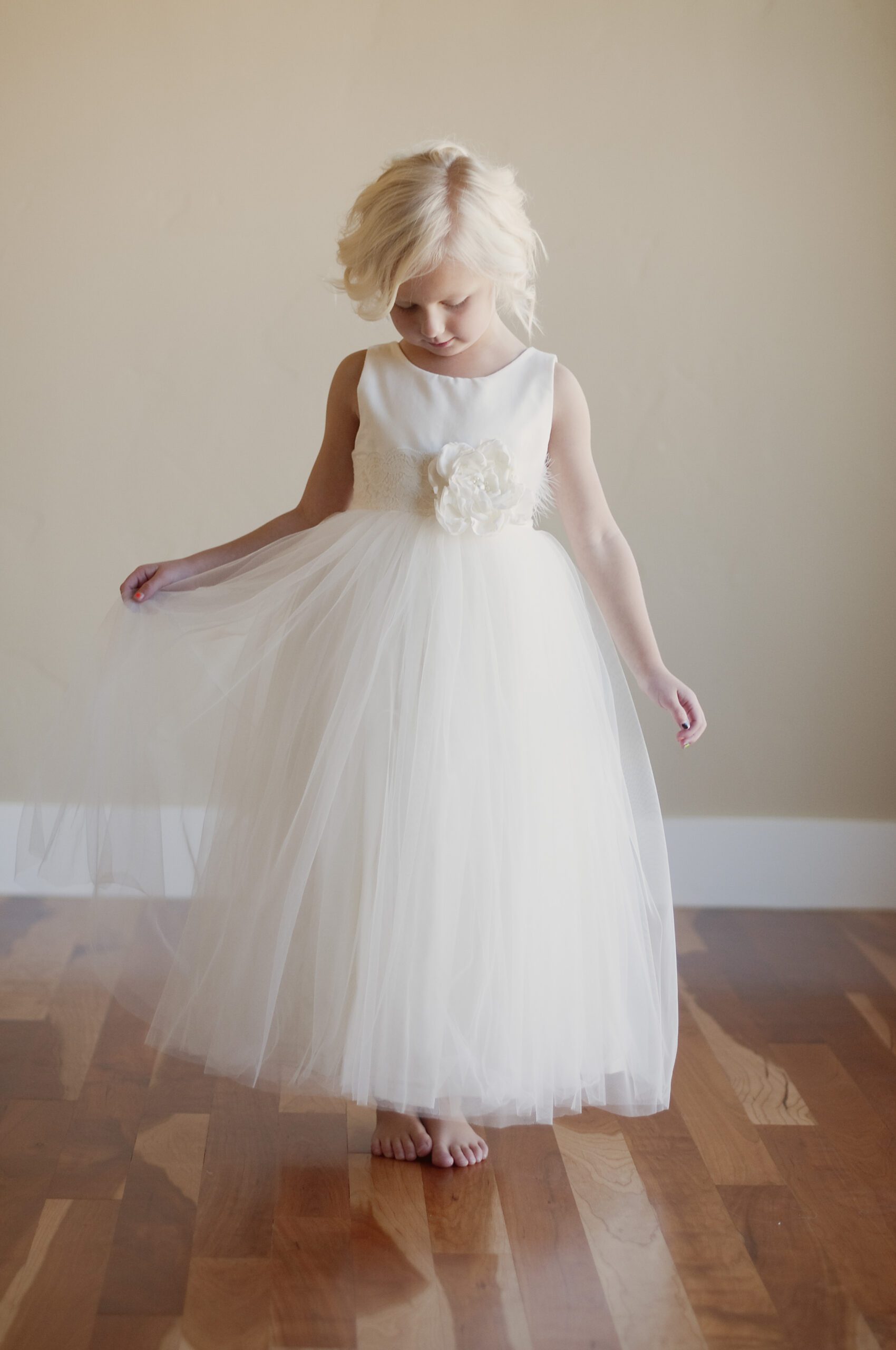 A photo of a little 5 year old girl wearing an ivory flower girl dress with a tulle skirt for twirling and a big organza flower