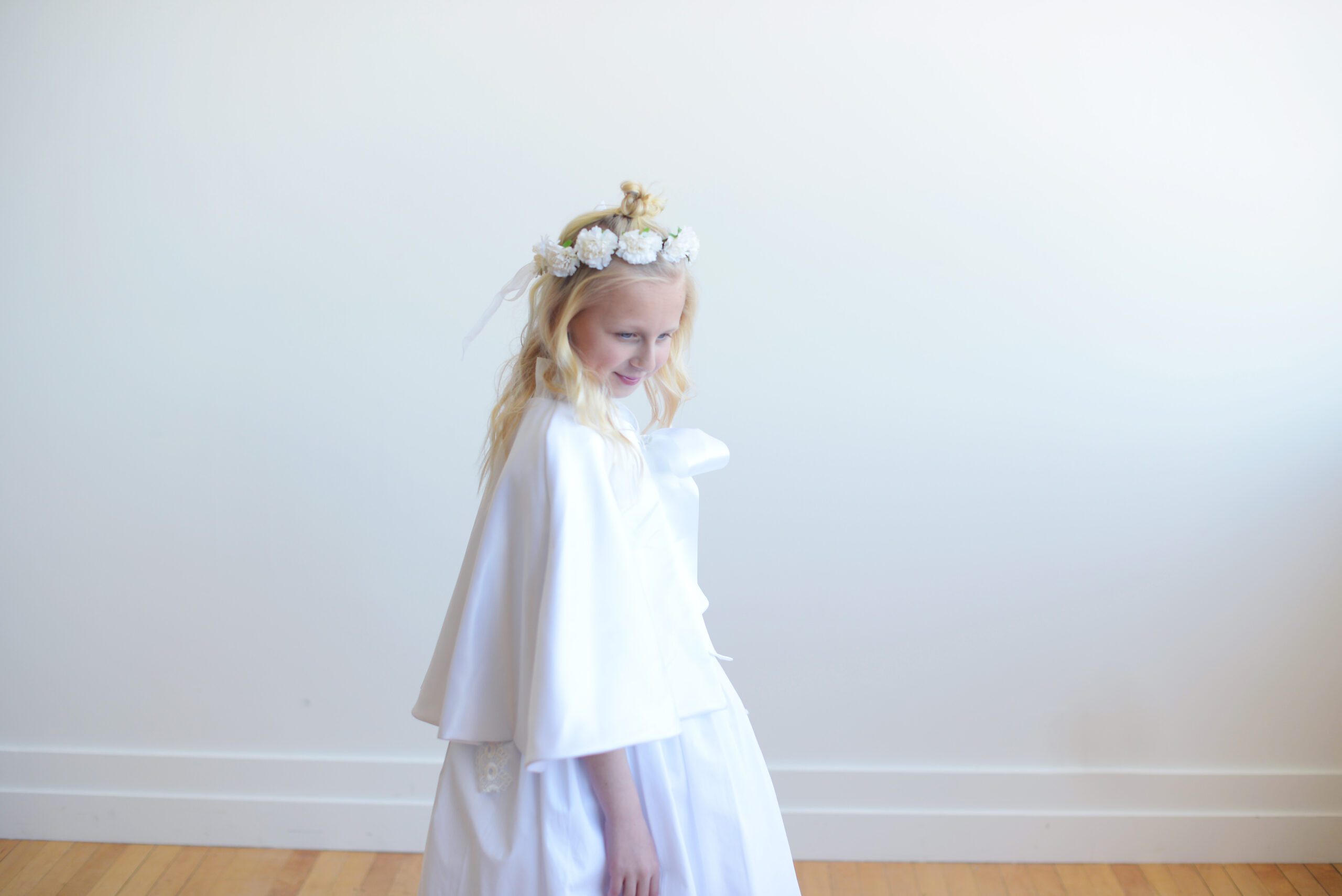 A photo of an 8 year old girl wearing a white communion dress with a lace sash and a communion cape znd veil