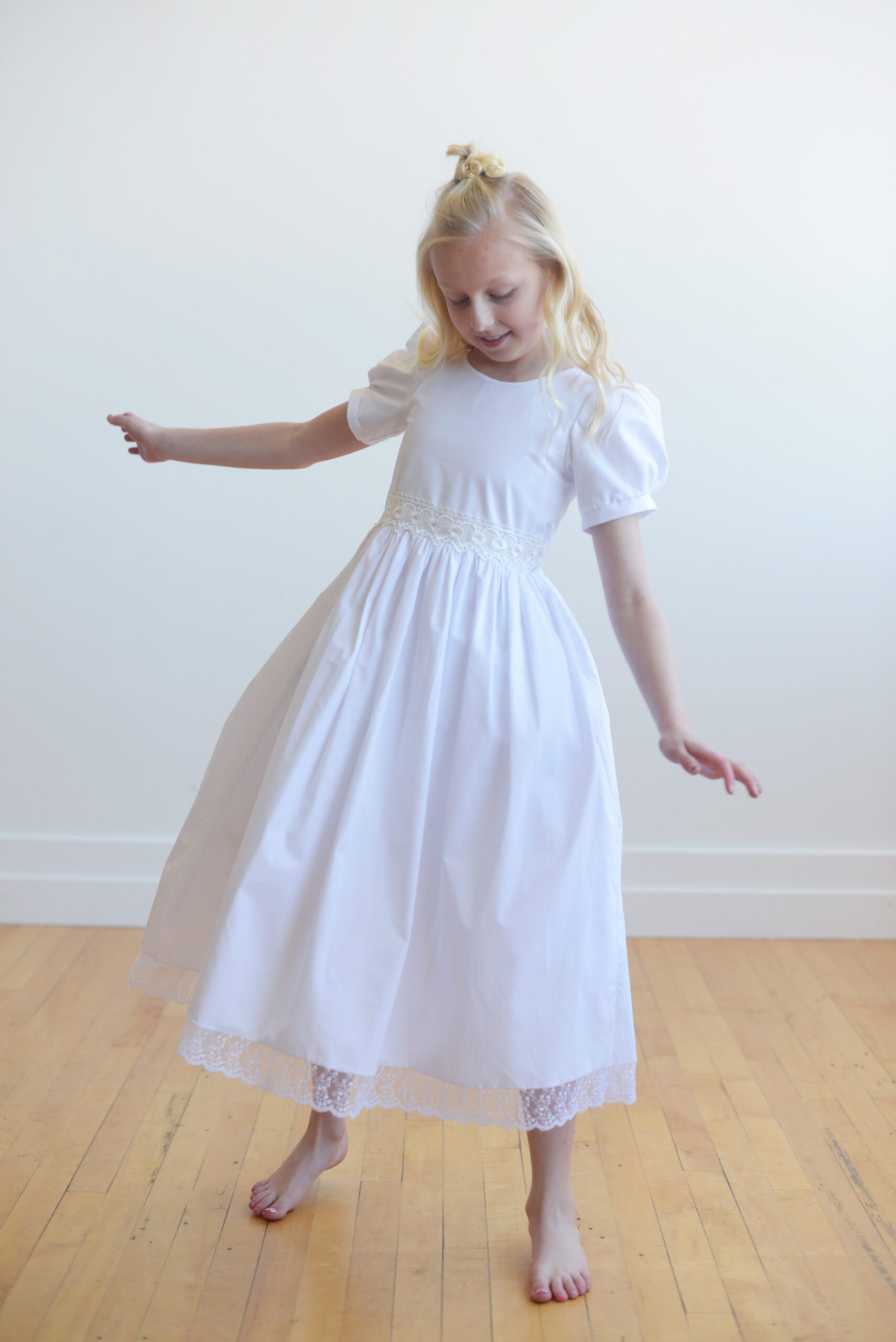 A photo of an 8 year old girl wearing a white communion dress with a lace sash