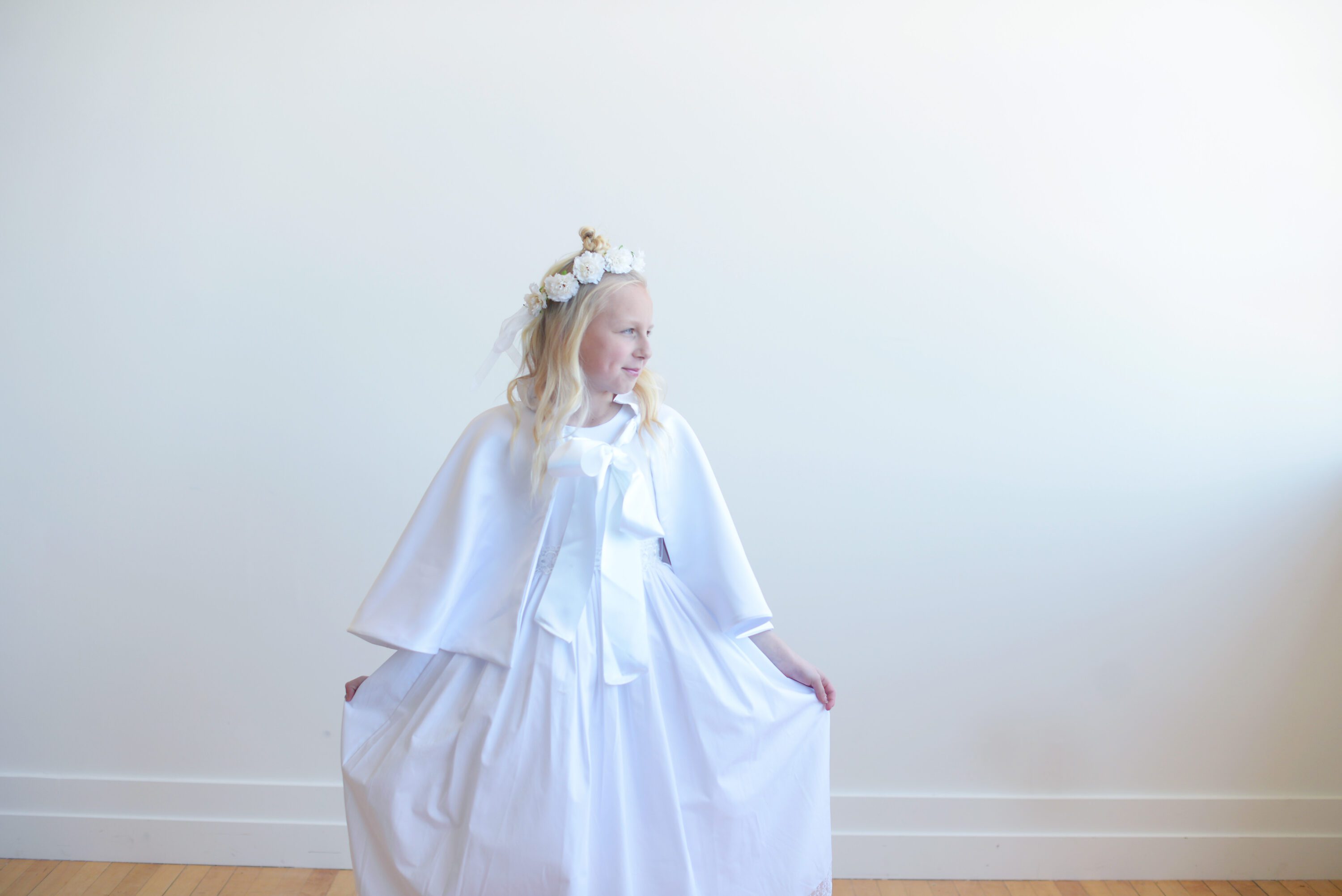 A photo of an 8 year old girl wearing a white communion dress with a lace sash and a communion cape