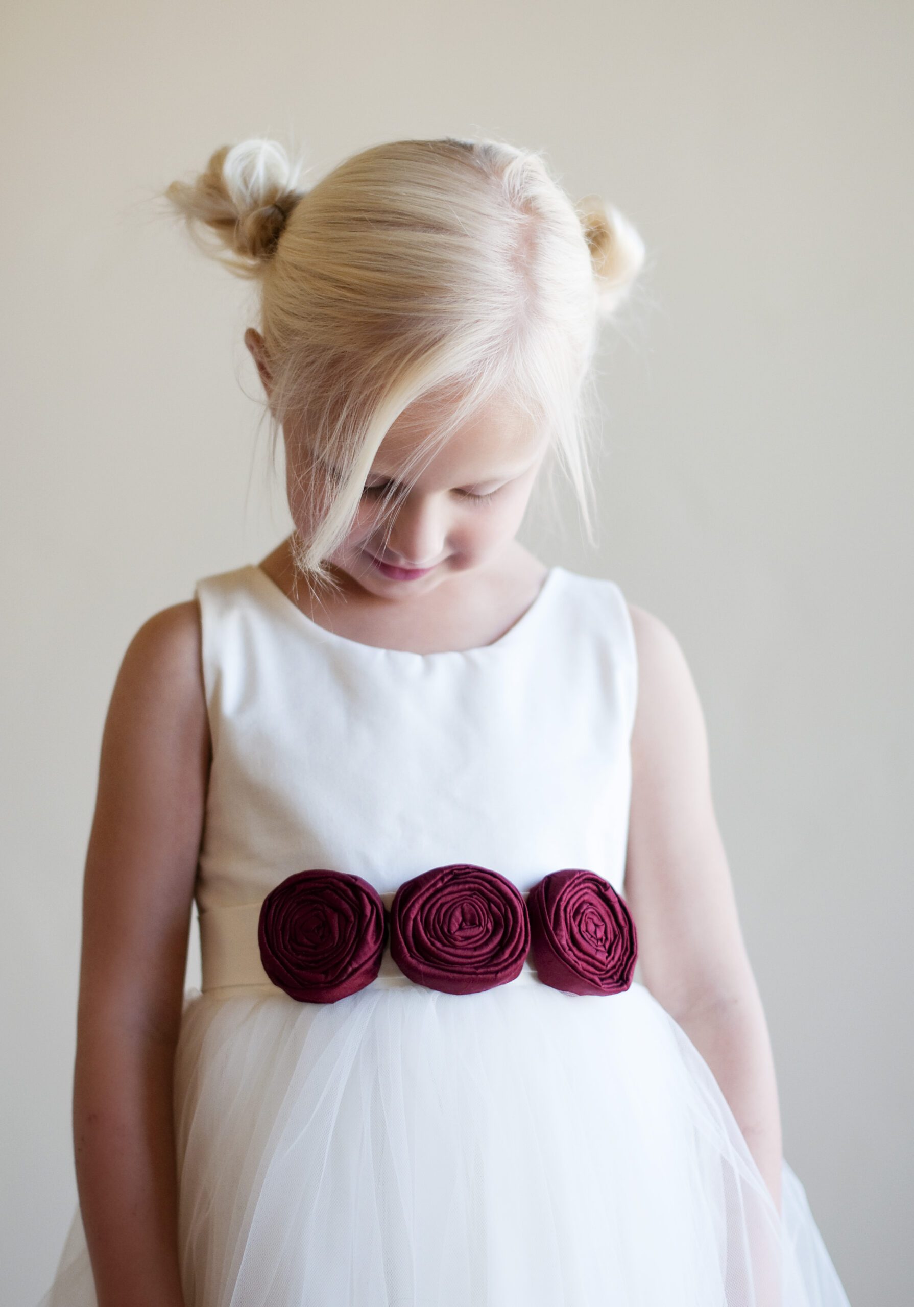 A photo of a white flower girl dress with a tulle skirt and red roses on the sash