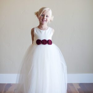 A photo of a white flower girl dress with a tulle skirt and red roses