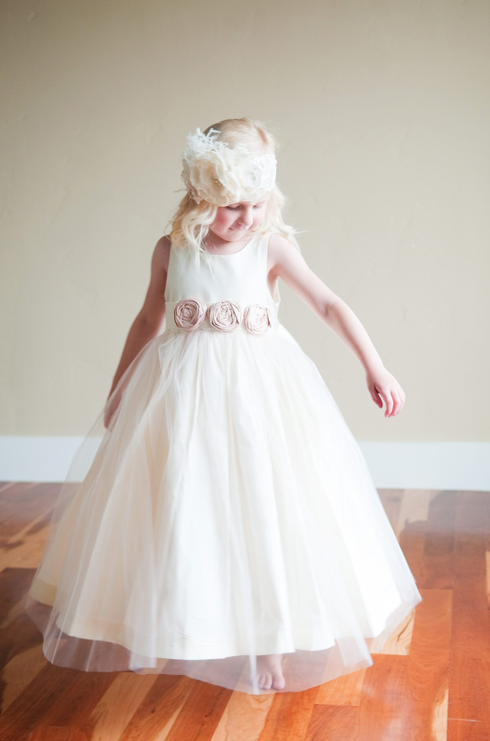 A photo of a young flower girl wearing an ivory cotton and tulle dress with pink silk roses