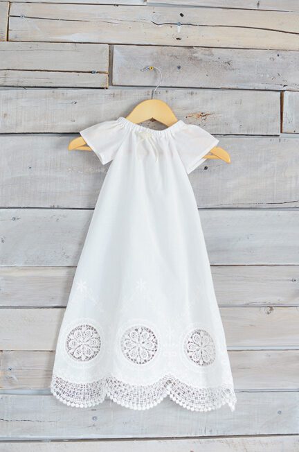 A photo of a white cotton christening gown with pretty lace detail at the hem
