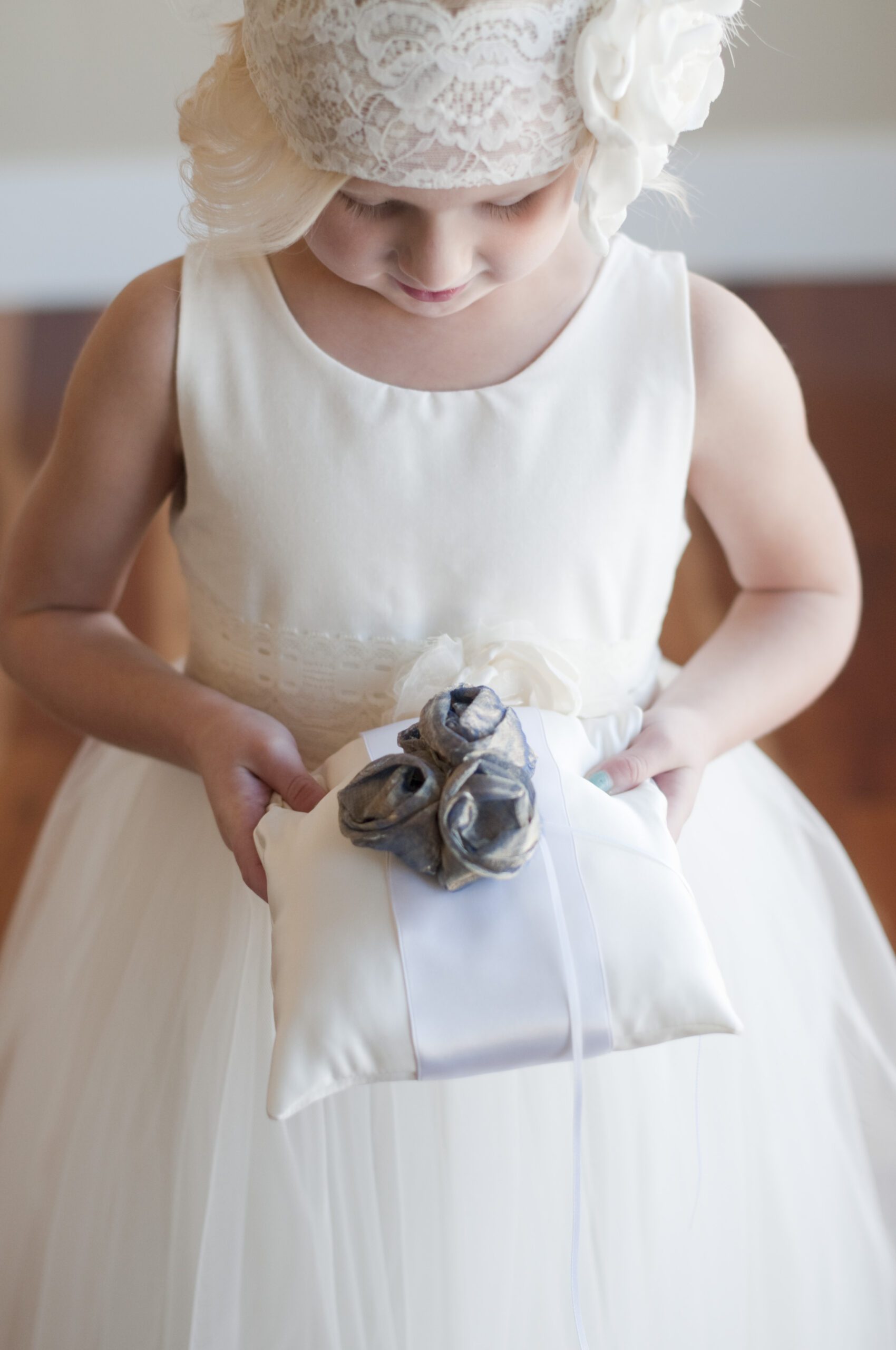 A photo of a flower girl holding a cotton ring pillow with an over sized flower and. ribbon with diamante