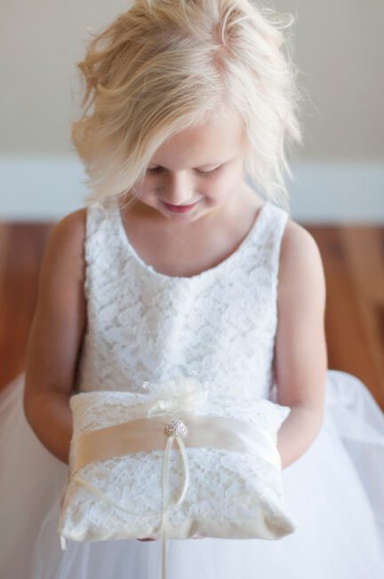 A photo of a flower girl holding a lace ring pillow